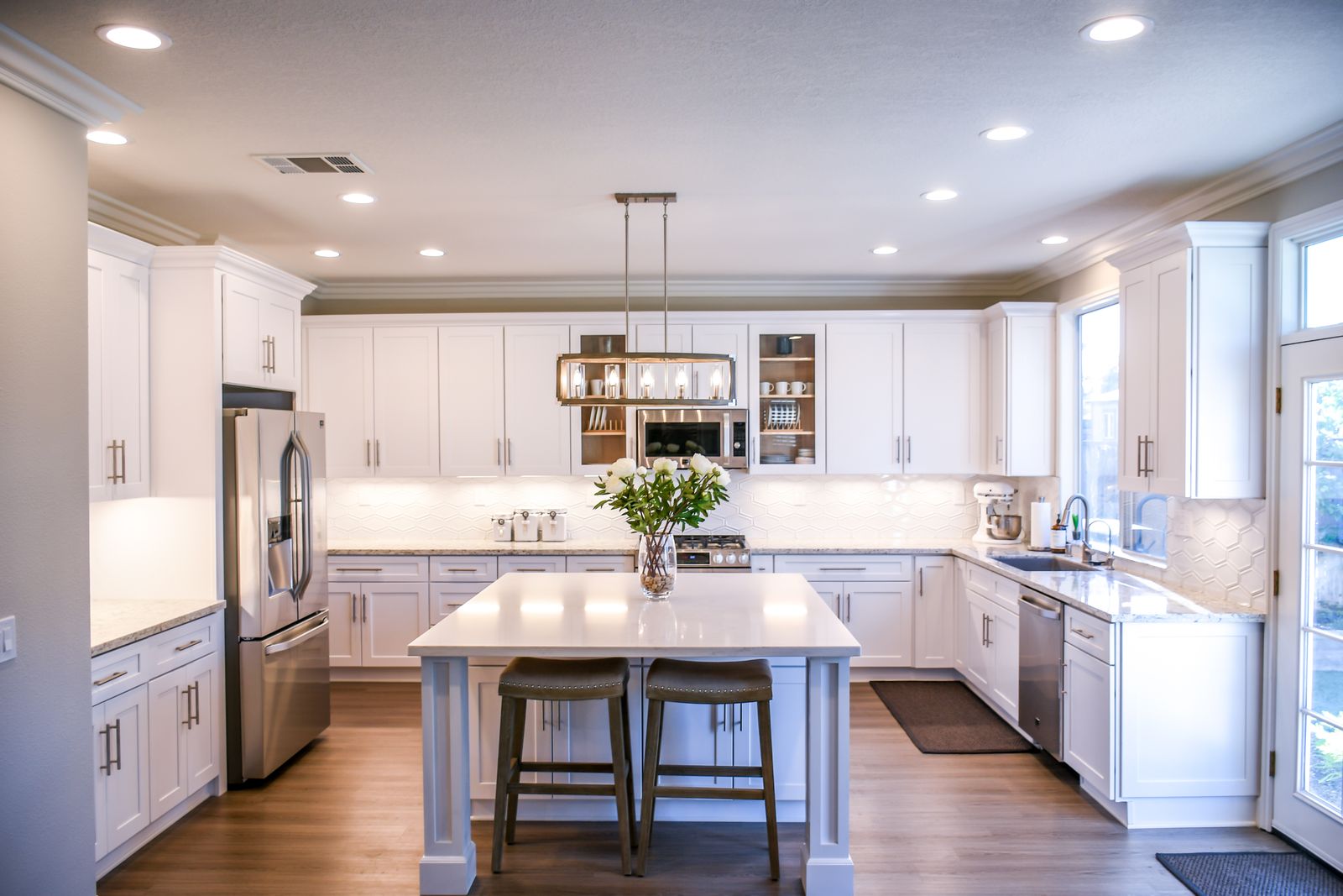 A bright remodeled kitchen with white custom cabinetry, stone counters, and an island